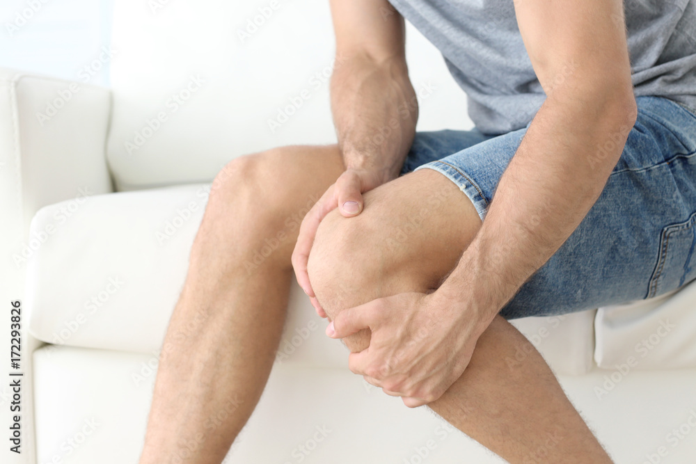Fototapeta premium Young man suffering from leg pain at home