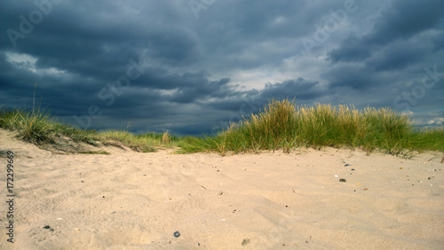 The approaching storm cloud on the beach with dunes and pure white sand