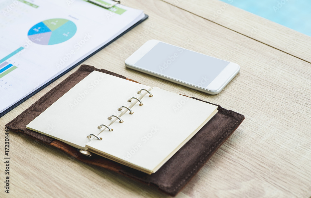Open blank organizer book with mobile phone and business chart on wood table at office. Open blank organizer book with mobile phone and business chart on wood table at office.