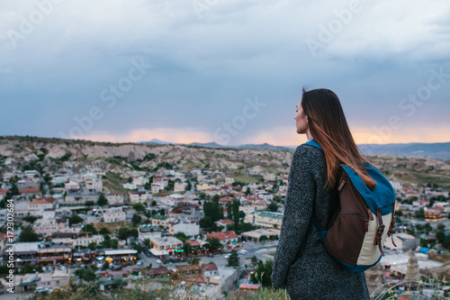 Young woman tourist from a high point looking at the sunset over the town and dreaming. Tourism, rest, vacation.