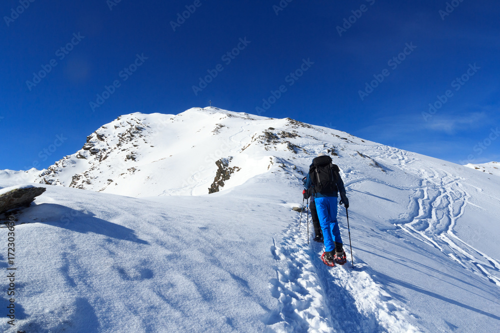 Group of people hiking on snowshoes and mountain snow panorama with summit cross in Stubai Alps, Austria