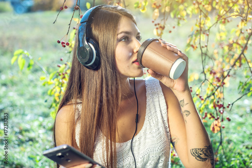 Woman listening to music in your phone wearing headphones on a Sunny day. Concept of audiobooks and student education