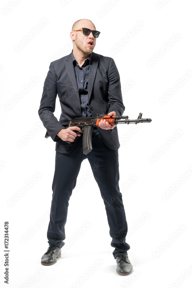 Bald man in a gray suit and sunglasses standing with a gun in his hand. Isolated Bald man in a gray suit and sunglasses standing with a gun in his hand. Isolated