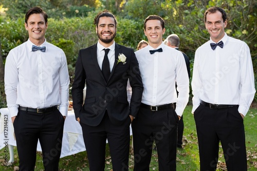 Portrait of groom and groomsmen standing with hands in pocket photo