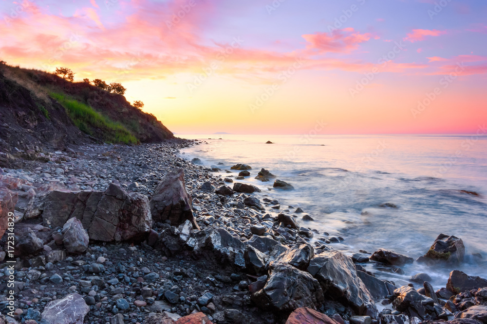 On the shore of the sea covered with stones opens a view on a beautiful landscape of a sunset. On the shore of the sea covered with stones opens a view on a beautiful landscape of a sunset.