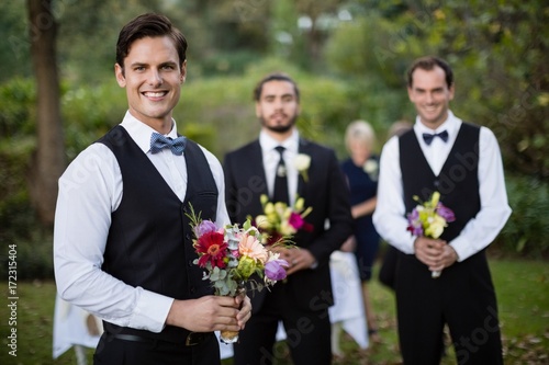 Bridegroom and best man standing with bouquet of flowers in