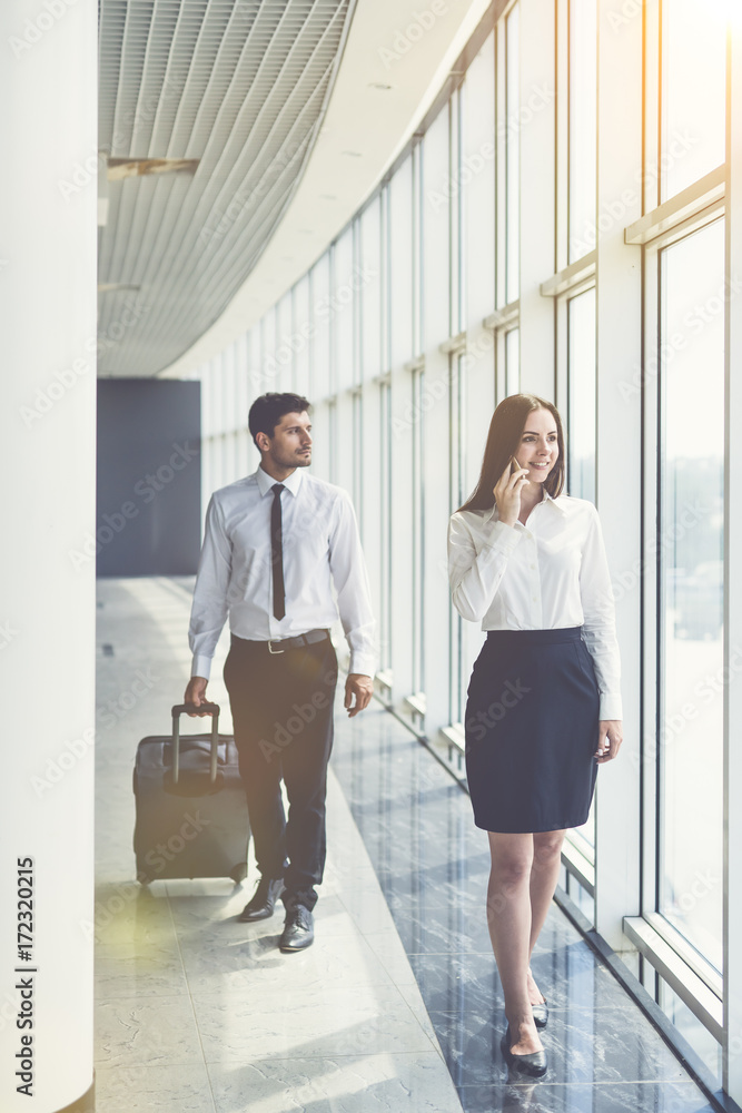 The business woman walk with a suitcase and phone in office hall The business woman walk with a suitcase and phone in office hall