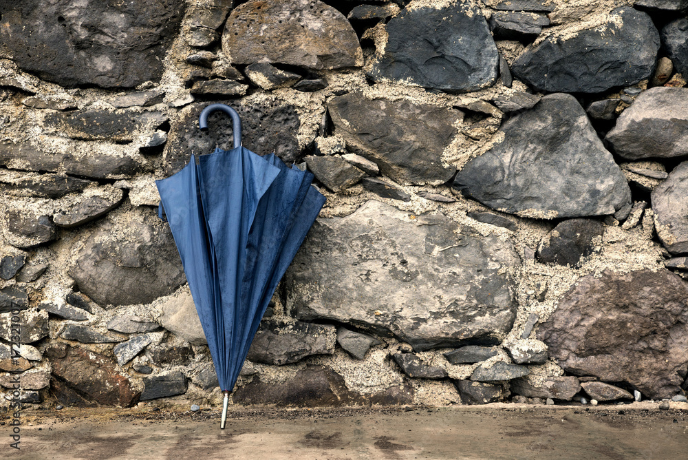 blue umbrella leaning on a stone wall