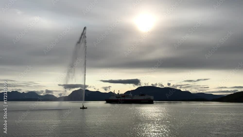 Fountain and Hurtigruten ferry in port in Harstad.Hurtigruten is a famous Norwegian cruise, ferry and cargo operator. The company was founded in 1893. Fountain and Hurtigruten ferry in port in Harstad.Hurtigruten is a famous Norwegian cruise, ferry and cargo operator. The company was founded in 1893.
