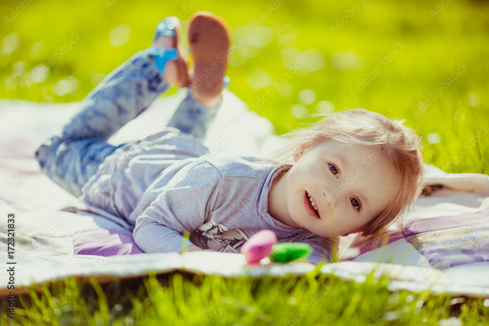 Happy little girl lies on white blanket on the lawn Happy little girl lies on white blanket on the lawn