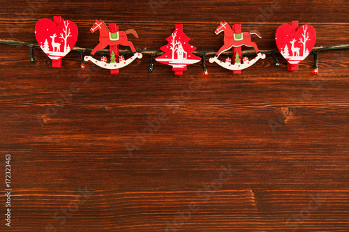 Red and white wooden Christmas decorations and Christmas lights on the brown wooden background, top view.