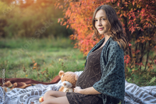 Expectant mother with a tummy sits on a blanket and tells stories to the baby. Concept of pregnancy and autumn harmony