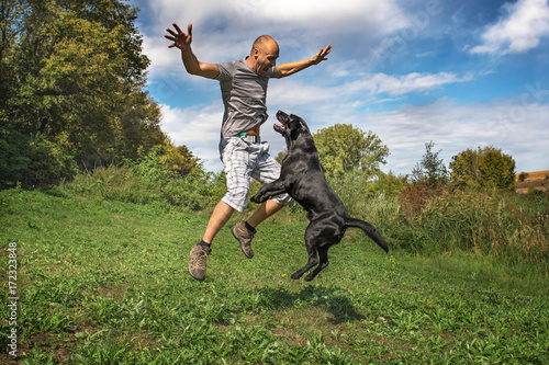 Man with black labrador are jumping in park.