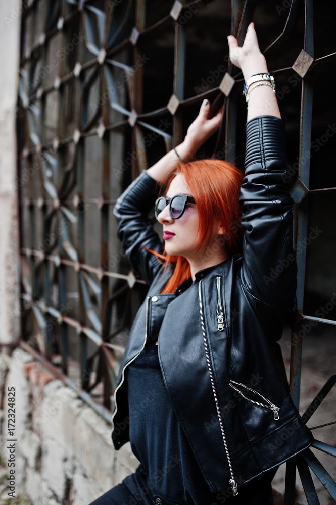 Naklejka premium Red haired stylish girl in sunglasses wear in black, against abadoned place.