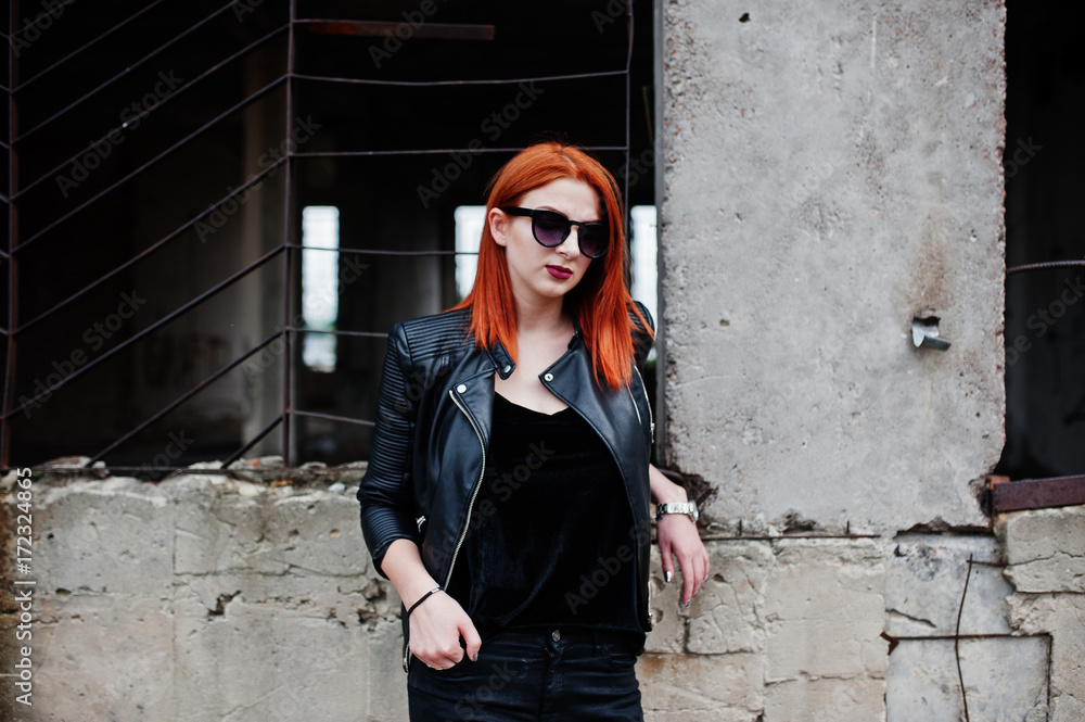Obraz premium Red haired stylish girl in sunglasses wear in black, against abadoned place.