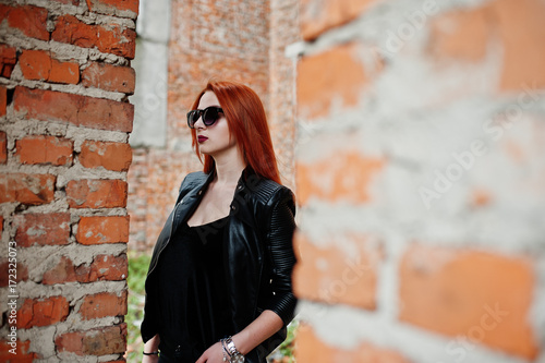 Red haired stylish girl in sunglasses wear in black, against abadoned place with brick walls. © AS Photo Family