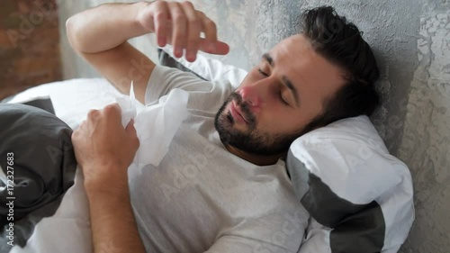 Sick millennial guy lying in bed and sneezing