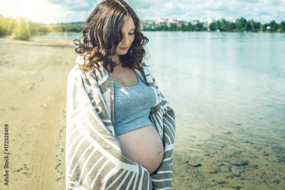 Pregnant walks on the river shore. Wrapped in a blanket