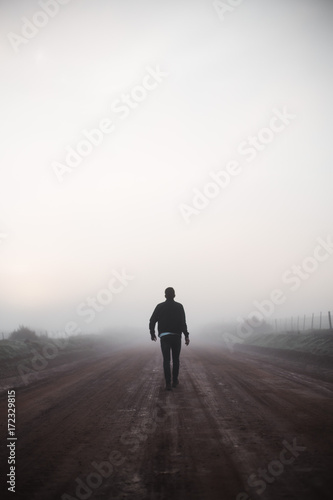 Silhouette man walking into mist on dirt road © Justin
