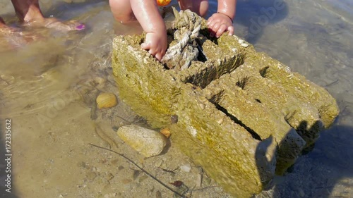 baby boy and his mother exploring concreete block laying in shallow sea water. in slow-motion hd  photo