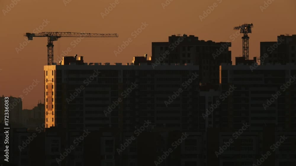 Construction cranes near residential apartments - view on sunrise