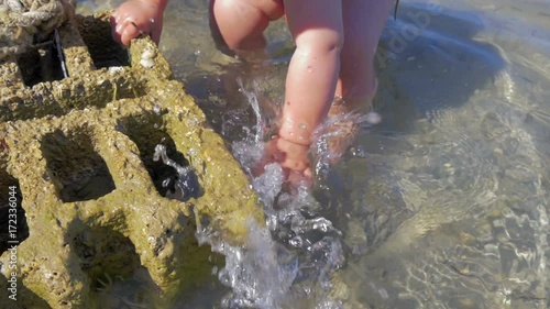 baby boy playing with sea water beside concreete block. slow-motion hd photo