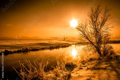 Fototapeta Winter river landscape, moody scenery with morning sun reflection in the water