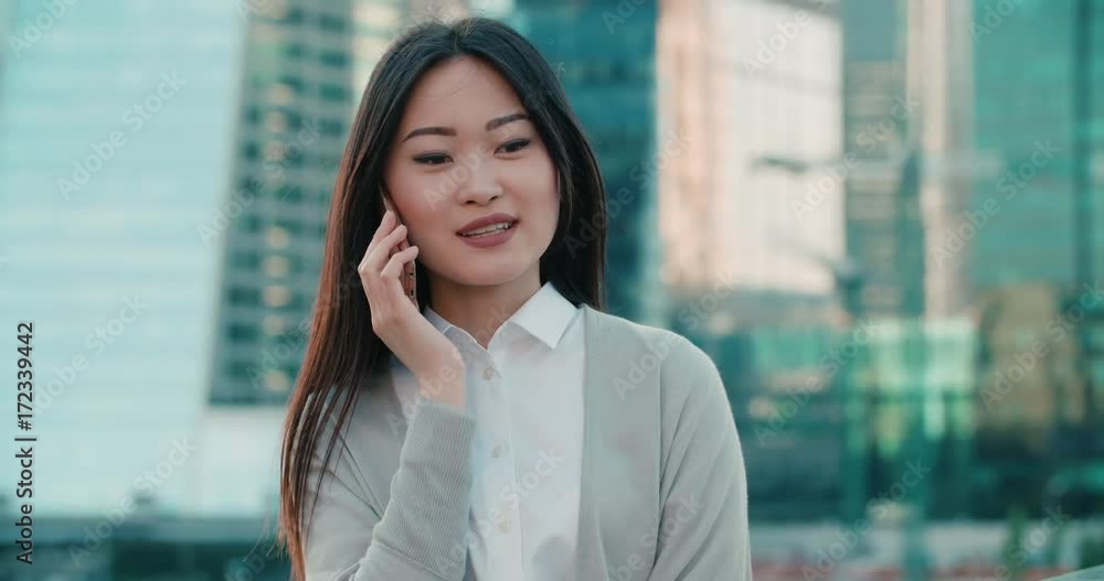 young successful Asian business woman portrait, woman talking on the phone in the background of a skyscraper, close-up young successful Asian business woman portrait, woman talking on the phone in the background of a skyscraper, close-up