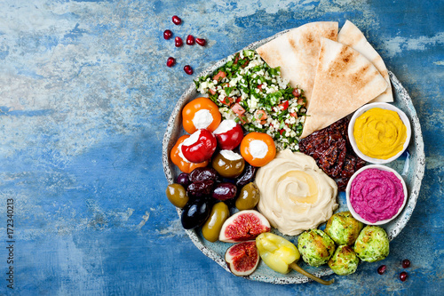 Middle Eastern meze platter with green falafel, pita, sun dried tomatoes, pumpkin and beet hummus, olives, stuffed peppers, tabbouleh, figs. Mediterranean appetizer party idea