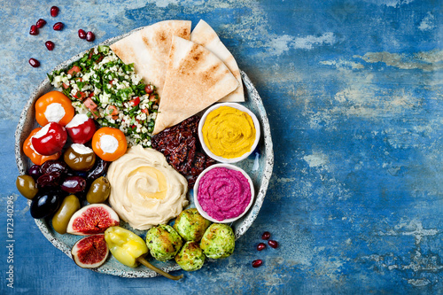 Middle Eastern meze platter with green falafel, pita, sun dried tomatoes, pumpkin and beet hummus, olives, stuffed peppers, tabbouleh, figs. Mediterranean appetizer party idea