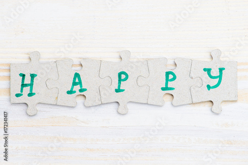 Word Happy made of four pieces of jigsaw puzzle on light wooden table, close-up
