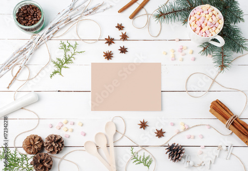 Fototapeta Naklejka Na Ścianę i Meble -  Frame composition of cocoa with marshmallow, cinnamon, anise stars, coffee seeds, fir tree, spoons and ingredients with clear card on center on white background. Copy space, autumn, kitchen concepts.