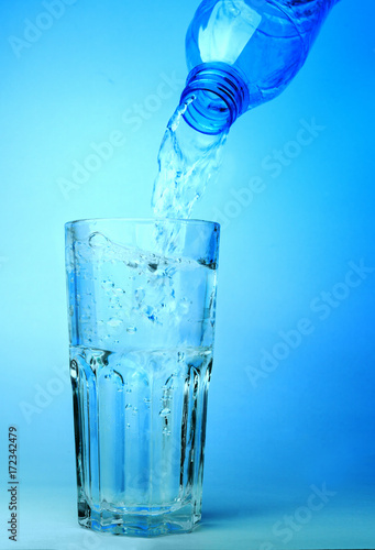 Close up shot : Pour water from plastic bottle in to the glass on blue backgroud