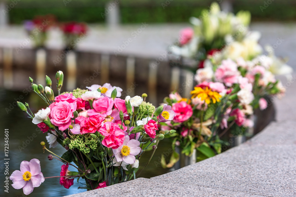 Flower bouquets for the dead beside a water pond at a memorial site.