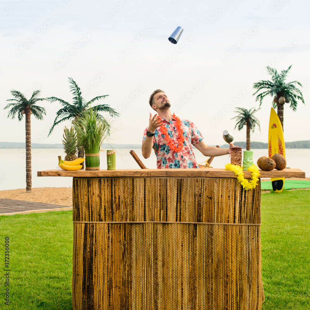 Handsome bartender standing near the bar counter and throws up a metal glass on the ocean