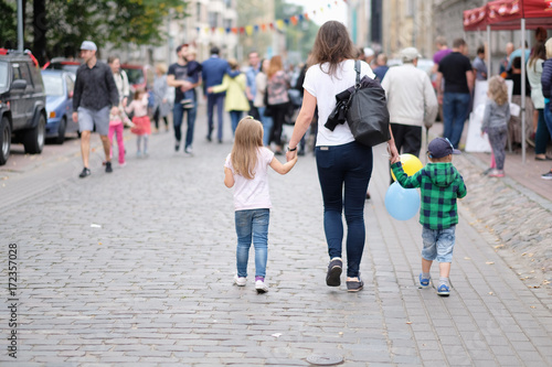 Children go with their mother along the street, holding their hands on the city holiday. Riga, Latvia. © Anna Jurkovska