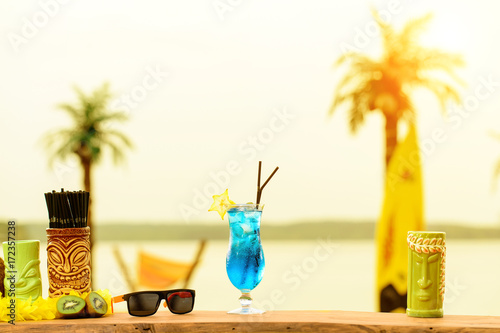 Bar counter on the beach at Hawaii. Glasses with cocktails, coconut, sun glasses lie on the table in rays of the sun. Concept of relaxing, preparation and summer