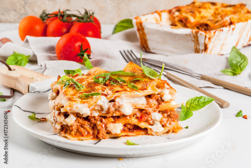 Italian food recipe. Dinner with classic lasagna bolognese with béchamel sauce, parmesan cheese, basil and tomatoes, on white marble table, coopy space