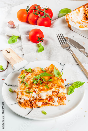 Italian food recipe. Dinner with classic lasagna bolognese with béchamel sauce, parmesan cheese, basil and tomatoes, on white marble table, coopy space
