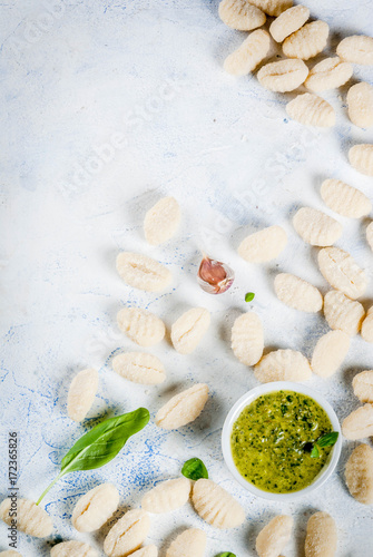 Raw uncooked homemade potato gnocchi with flour, grated parmesan cheese, basil and pesto sauce. On concrete light blue background, copy space top view