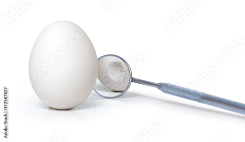 Broken egg with dental mirror on white background. Creative idea