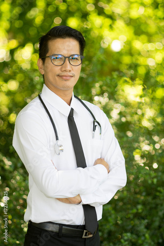 Portrait of asian doctor smiling with glasses and stethoscope in green nature background.