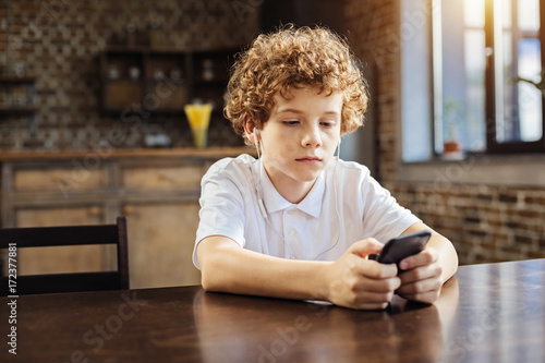 Calm chestnut haired boy choosing music on phone