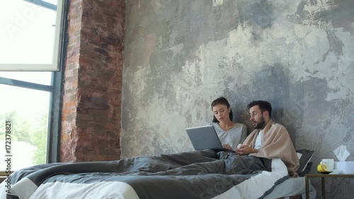Young married couple working on laptop in bed