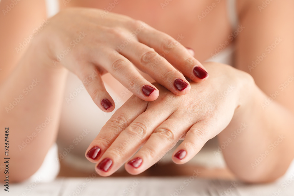 Women's hands with red manicure to apply the cream