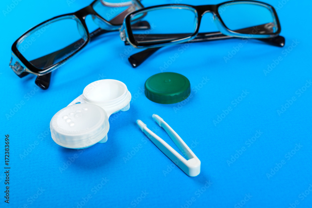 glasses, contact lenses in containers and tweezers on blue background glasses, contact lenses in containers and tweezers on blue background