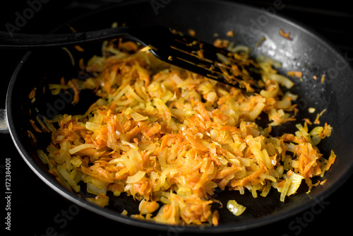 Chopped onions and carrots fry in vegetable oil in a frying pan on a black background, closeup