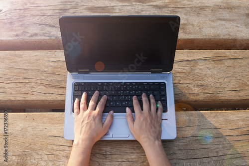 Unrecognizable woman working outdoor on her laptop. Sunset positive vibe. Relaxed business. Notebook mockup , display replaceable with your design.