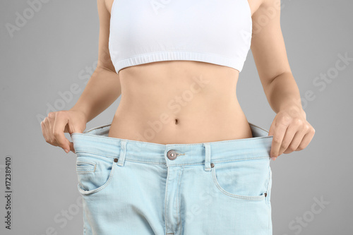 Young woman in oversized jeans on gray background, closeup. Diet concept