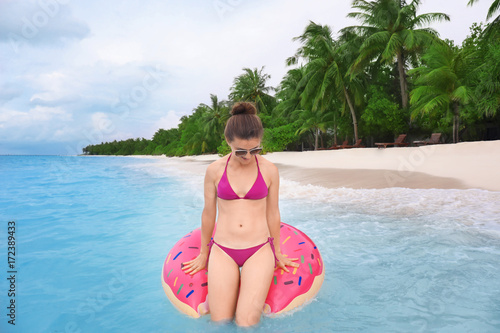 Beautiful young woman bathing with colorful inflatable donut at resort